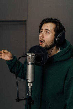 Photo for Singer with headphones and microphone emotionally recording a new song in professional recording studio - Royalty Free Image