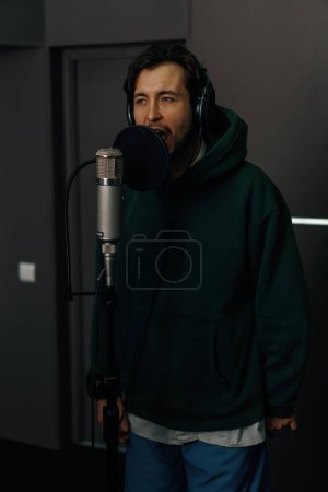 Foto de Cantante con auriculares y micrófono grabando emocionalmente una nueva canción en un estudio de grabación profesional - Imagen libre de derechos