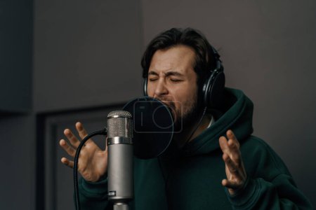 Téléchargez les photos : Chanteur avec écouteurs et microphone enregistrement émotionnel d'une nouvelle chanson en studio d'enregistrement professionnel - en image libre de droit