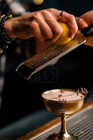 Foto de Las manos masculinas de un camarero frotan la cáscara de una fruta naranja para un cóctel con una herramienta especial para rallar - Imagen libre de derechos