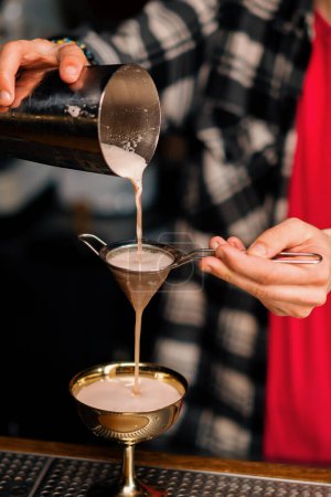Téléchargez les photos : Le barman verse le cocktail fini dans un beau verre de shaker à travers une passoire à alcool - en image libre de droit