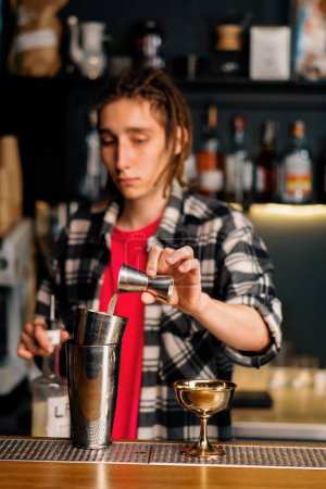 Foto de Un camarero experimentado vierte líquido en una coctelera con la ayuda de un jigger prepara un cóctel en el club nocturno - Imagen libre de derechos