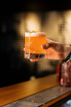 Foto de Un primer plano de un invitado de bar sosteniendo preparado sabroso cóctel alcohólico agrio melocotón en su mano - Imagen libre de derechos