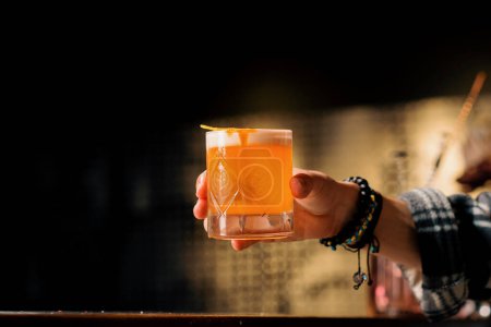 A close-up of a bar guest holding ready-made tasty peach sour alcoholic cocktail in his hand