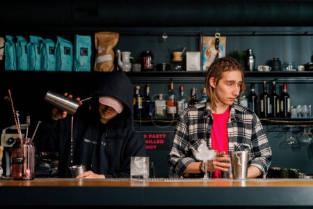 Téléchargez les photos : Deux jeunes barmans préparant des cocktails alcoolisés au bar mélangeant des ingrédients travaillant par paires à la fête - en image libre de droit