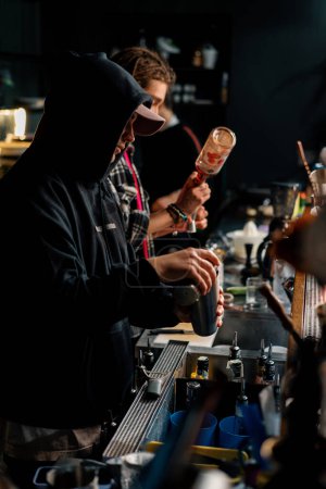 Foto de Dos camareros jóvenes preparando cócteles alcohólicos en el bar mezclando ingredientes trabajando en parejas en la fiesta - Imagen libre de derechos