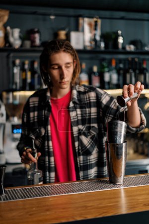 Téléchargez les photos : Un barman expérimenté verse du liquide dans un shaker à l'aide d'un jigger prépare un cocktail en boîte de nuit - en image libre de droit