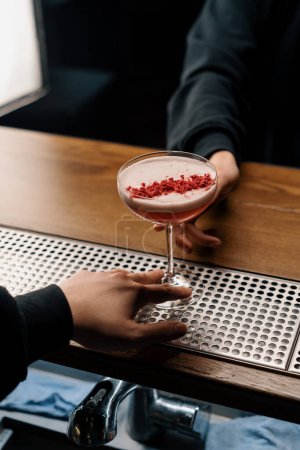 Foto de El camarero da un delicioso cóctel de ponche de leche de frambuesa rosa recién preparado para el cliente desde el mostrador del bar - Imagen libre de derechos