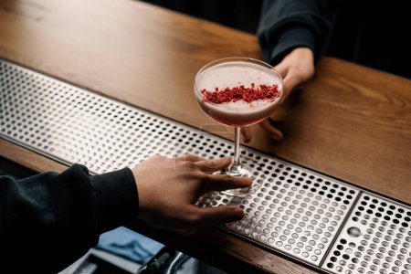Photo for The bartender gives a delicious pink freshly prepared raspberry milk punch cocktail to the client from bar counter - Royalty Free Image