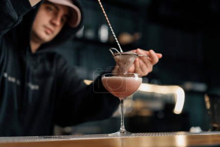 Téléchargez les photos : Boisson rose goutte à goutte à travers un tamis Mains avec un tamis et cuillère Barman prépare cocktail punch au lait - en image libre de droit