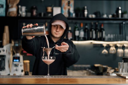 Téléchargez les photos : Le barman verse le cocktail fini dans un verre transparent à partir d'un shaker à travers l'alcool passoire - en image libre de droit