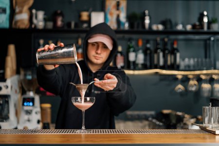 Foto de El camarero vierte el cóctel terminado en un vaso transparente de una coctelera a través del alcohol colador - Imagen libre de derechos