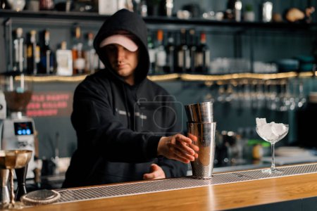 Photo for The bartender begins to prepare an alcoholic cocktail takes shaker from the bar in his hand - Royalty Free Image