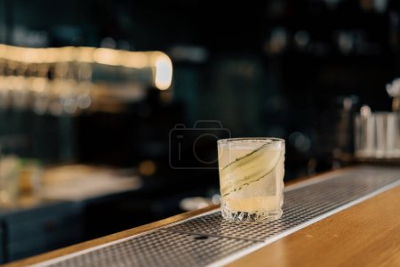 Téléchargez les photos : Fraîchement préparé gin garden cocktail alcoolisé avec une trancheuse de concombre se trouve sur le comptoir du bar dans le bar club - en image libre de droit