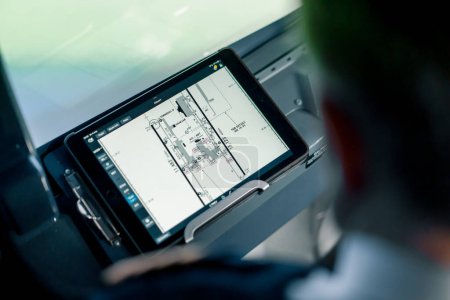 Téléchargez les photos : Le pilote tient une tablette dans ses mains, regarde la route de vol et choisit le lieu d'atterrissage de l'avion - en image libre de droit