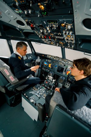 Téléchargez les photos : Un pilote expérimenté instruit un jeune élève avant un vol d'entraînement dans le poste de pilotage d'un simulateur d'aéronef - en image libre de droit
