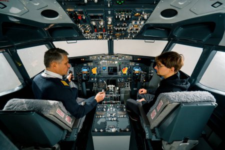 Téléchargez les photos : Un pilote expérimenté instruit un jeune élève avant un vol d'entraînement dans le poste de pilotage d'un simulateur d'aéronef - en image libre de droit