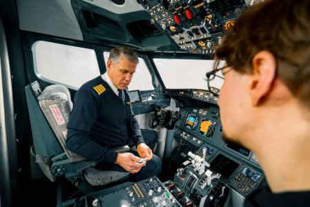 An experienced pilot instructs a young student and shows a small model airplane in the cockpit of aero simulator