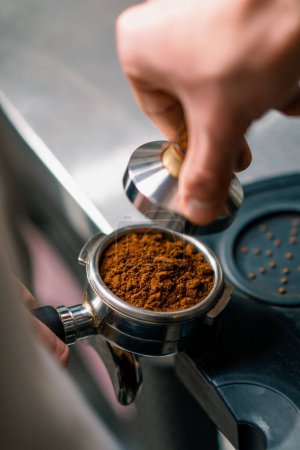 Téléchargez les photos : Un barista professionnel dans un café prépare le café moulu en tamponnant les grains de café moulus frais close-up - en image libre de droit