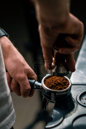 Photo for A professional barista in coffee shop prepares ground coffee by tamping fresh ground coffee beans close-up - Royalty Free Image