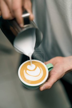 Foto de Barista haciendo arte latte en una cafetería Manos masculinas vertiendo vapor de leche en una taza de capuchino con patrón - Imagen libre de derechos