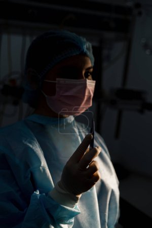 Photo for Nurse or surgeon in sterile glove holding scalp surgical instrument in hand during operation dark room - Royalty Free Image