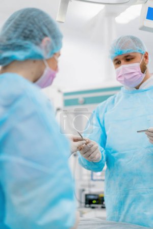 Foto de Una enfermera en un guante estéril manos cuero cabelludo instrumentos quirúrgicos a un cirujano durante una operación en el hospital - Imagen libre de derechos