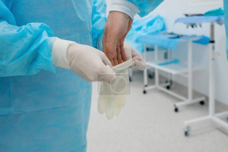 Foto de Enfermera ayuda al cirujano a ponerse guantes estériles antes de la cirugía uniforme en la cirugía de preparación de quirófano - Imagen libre de derechos