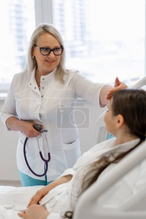 Foto de Una doctora en un hospital comprueba el estado de una paciente joven mide la temperatura con la mano - Imagen libre de derechos