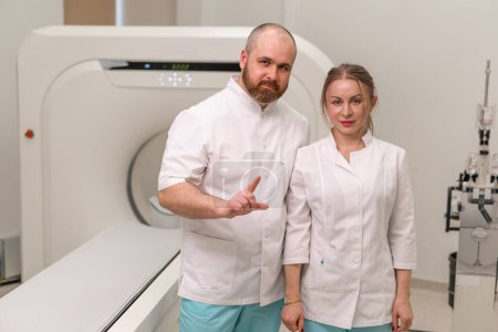 Photo for Smiling and satisfied doctors in uniform posing near magnetic resonance imaging machine concept professions and medicine - Royalty Free Image