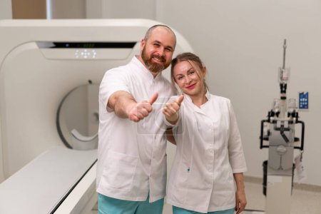 Photo for Smiling and satisfied doctors in uniform posing near magnetic resonance imaging machine concept professions and medicine - Royalty Free Image
