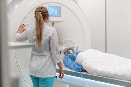 Téléchargez les photos : Un radiologue professionnel dans une clinique médicale surveille un patient subissant une procédure d'imagerie par résonance magnétique - en image libre de droit
