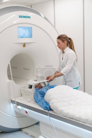 Téléchargez les photos : Un radiologue dans une clinique médicale place l'appareil sur la tête du patient avant la procédure d'imagerie par résonance magnétique cérébrale - en image libre de droit