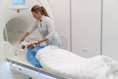 Foto de Un radiólogo en una clínica médica coloca el dispositivo en la cabeza del paciente antes del procedimiento de resonancia magnética cerebral - Imagen libre de derechos
