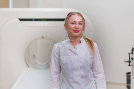 Téléchargez les photos : Sourire belle femme médecin CT radiologue dans le bureau de tomodensitométrie attendre les patients avant de commencer le travail - en image libre de droit