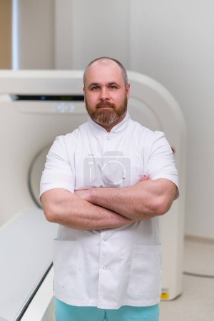 Téléchargez les photos : Médecin barbu grave CT radiologue dans le bureau de tomodensitométrie attendre les patients avant de commencer le travail - en image libre de droit