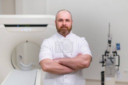 Téléchargez les photos : Médecin barbu grave CT radiologue dans le bureau de tomodensitométrie attendre les patients avant de commencer le travail - en image libre de droit