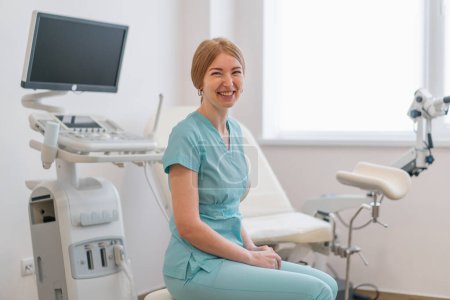 Photo for Smiling doctor gynecologist sits in gynecological office near ultrasound machine and gynecological chair waiting patients - Royalty Free Image