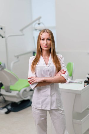 Foto de Retrato de la hermosa joven sonriente dentista médico de pie en el consultorio dental antes del procedimiento - Imagen libre de derechos