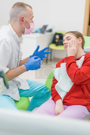Foto de Paciente femenina molesta en la cita con el dentista se queja dolor de muelas y caries sosteniendo sus mejillas consultorio dental - Imagen libre de derechos