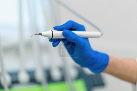 Téléchargez les photos : Dentiste professionnel tenant des outils de travail pour enlever le tartre dans la main gantée avant l'intervention en clinique fermer - en image libre de droit