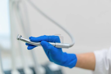 Téléchargez les photos : Dentiste professionnel tenant la pièce à main de la turbine dentaire de l'outil de travail dans la main gantée avant l'intervention en clinique gros plan - en image libre de droit
