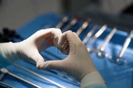 Photo for The doctor shows the heart sign with his hands after the operation on background of surgical instruments - Royalty Free Image