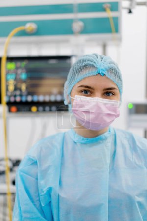 Photo for Portrait of a young female doctor in a mask and sterile protective clothing standing in the operating room after  operation - Royalty Free Image