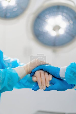 Téléchargez les photos : Médecins chirurgiens en gants tenant la main après la chirurgie soutenir les collègues dans la salle d'opération - en image libre de droit