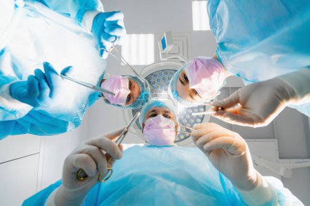 Foto de Grupo de médicos cirujanos y enfermeras que sostienen instrumentos quirúrgicos de bisturí durante la operación en la vista inferior del hospital - Imagen libre de derechos