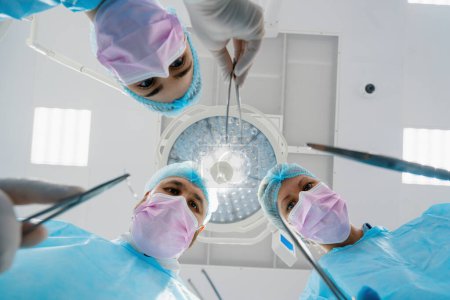 Téléchargez les photos : Groupe de médecins chirurgiens et infirmières tenant des scalpels instruments chirurgicaux pendant l'opération à l'hôpital vue du bas - en image libre de droit