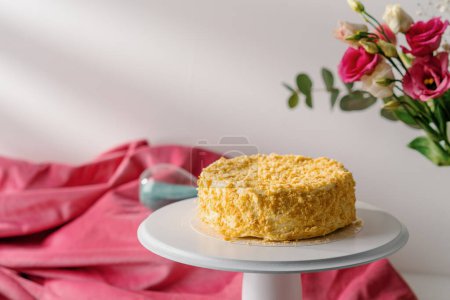 Téléchargez les photos : Délicieux gâteau Napoléon fraîchement préparé à partir de pâte feuilletée sur un stand blanc sur fond lumineux de fleurs concept de dessert - en image libre de droit