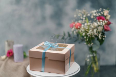 Photo for A packed delicious cake in a gift box with a bow stands on stand on a background of flowers - Royalty Free Image