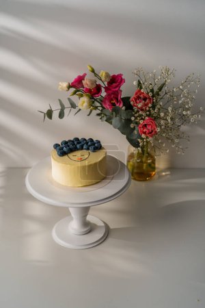 Téléchargez les photos : Délicieux gâteau biscuit bento fraîchement préparé décoré avec des baies se tient sur un stand sur fond blanc avec des fleurs - en image libre de droit